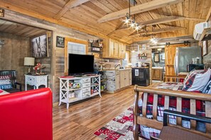 A cozy cabin interior with wooden walls, a television, a kitchen area, and a red chair.