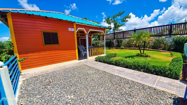 A red building with a blue roof, a covered porch with chairs, and a gravel pathway leading to it.