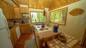 Une cuisine en bois équipée d’une cuisinière, d’un évier et de meubles de rangement en bois. Il y a des fenêtres donnant sur des arbres, et un motif décoratif représentant des poissons orne le mur.