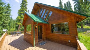 Une cabane en bois dotée d’une terrasse, de grandes fenêtres et d’un toit végétalisé.
