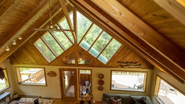 Une pièce spacieuse avec un plafond haut, des fenêtres de toit, un ventilateur de plafond et une vue sur l’extérieur.
