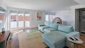 A modern living room with a light blue sofa, a glass coffee table, and a wicker chair. - Minty House (Setúbal)