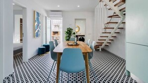 A modern dining area with a wooden table and blue chairs, a patterned floor, and a staircase with wooden steps. - Minty House (Setúbal)