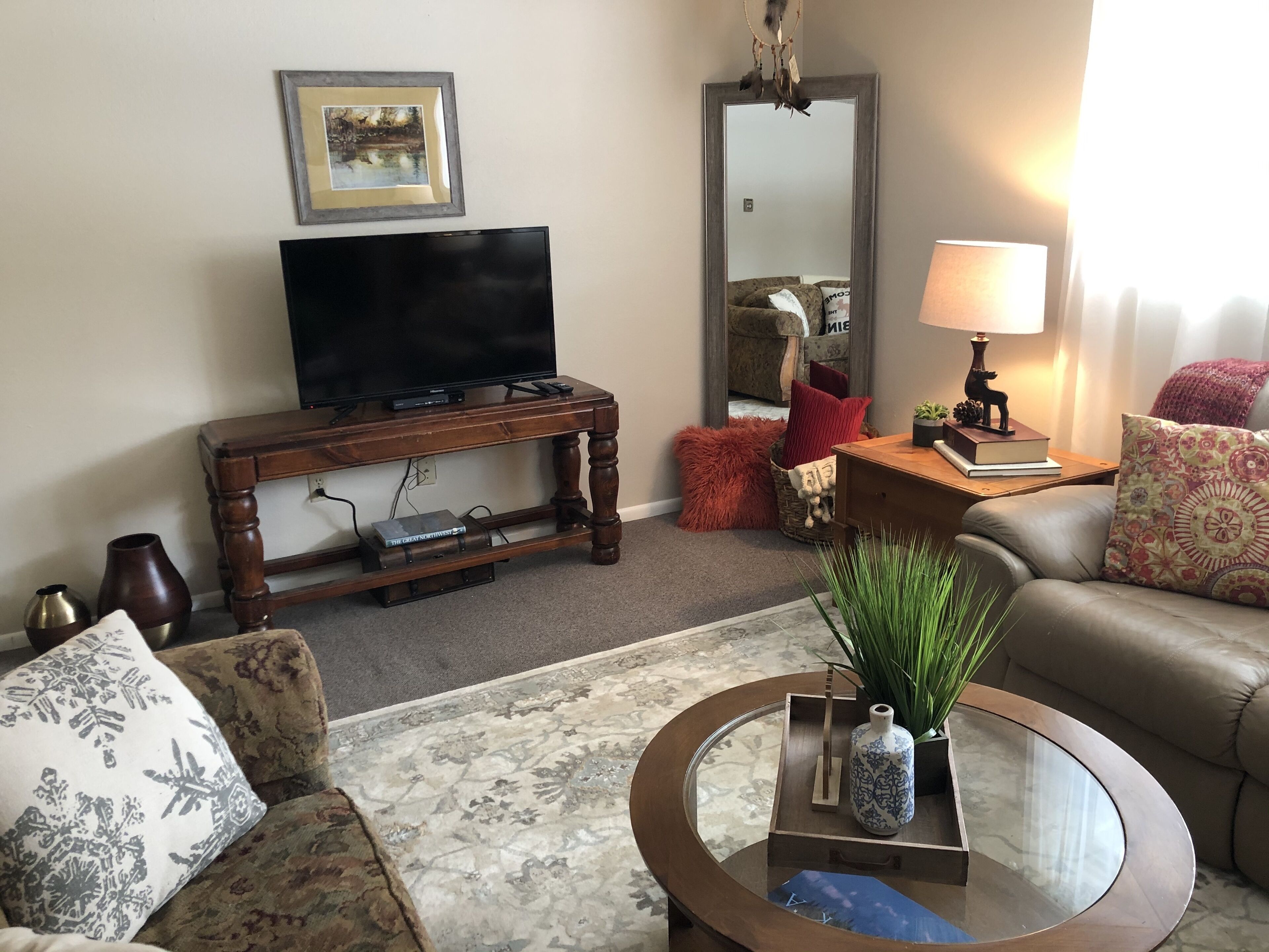 A living room with a television on a wooden stand, a sofa, a coffee table with decorative items, and a mirror on the wall.