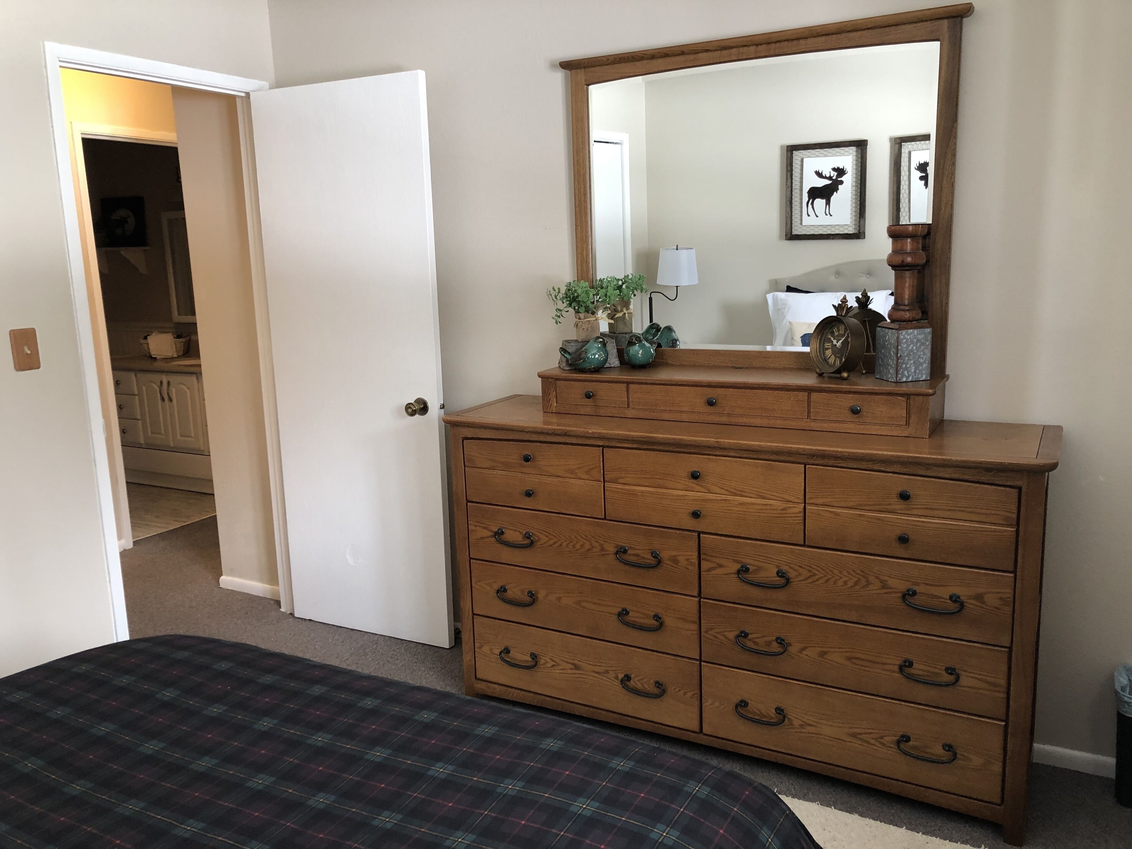 Una camera da letto con una cassettiera in legno, un letto con copriletto a quadri, uno specchio e una porta che dà su un corridoio.