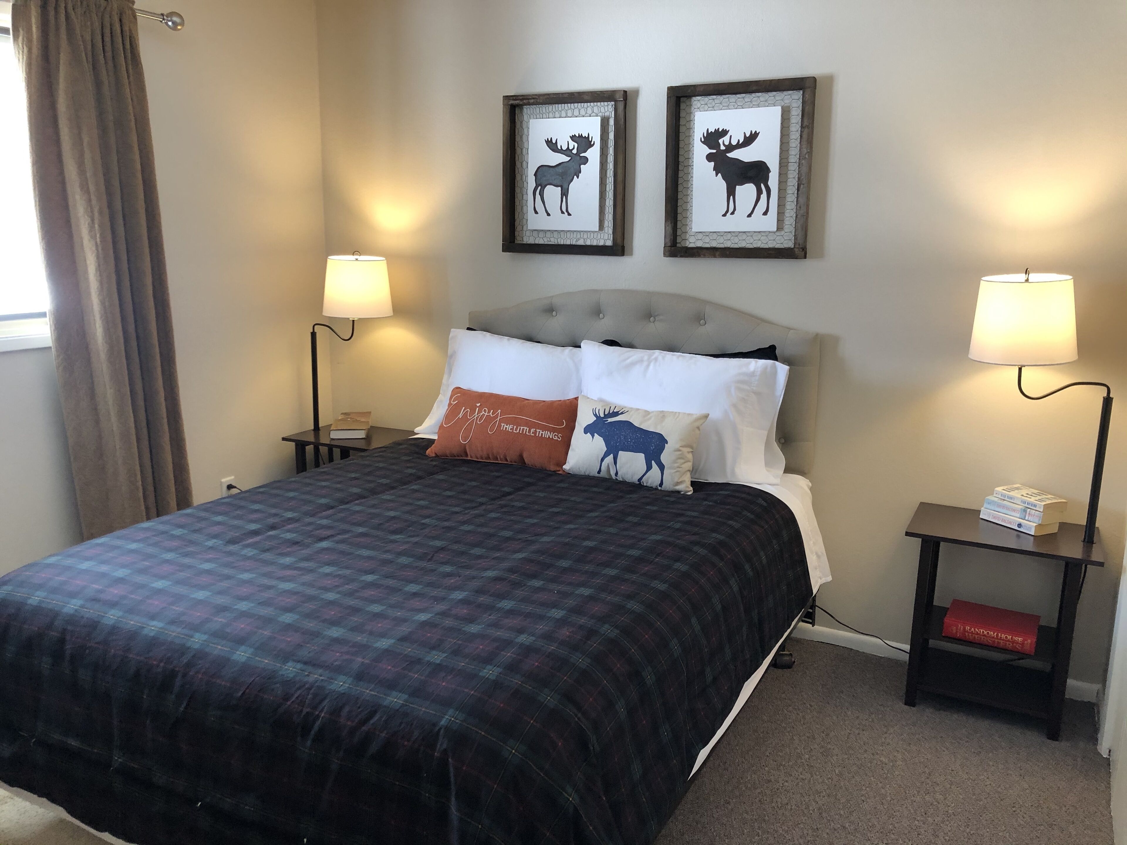 A neatly made bed with a plaid bedspread, two framed animal silhouettes on the wall, and bedside lamps.