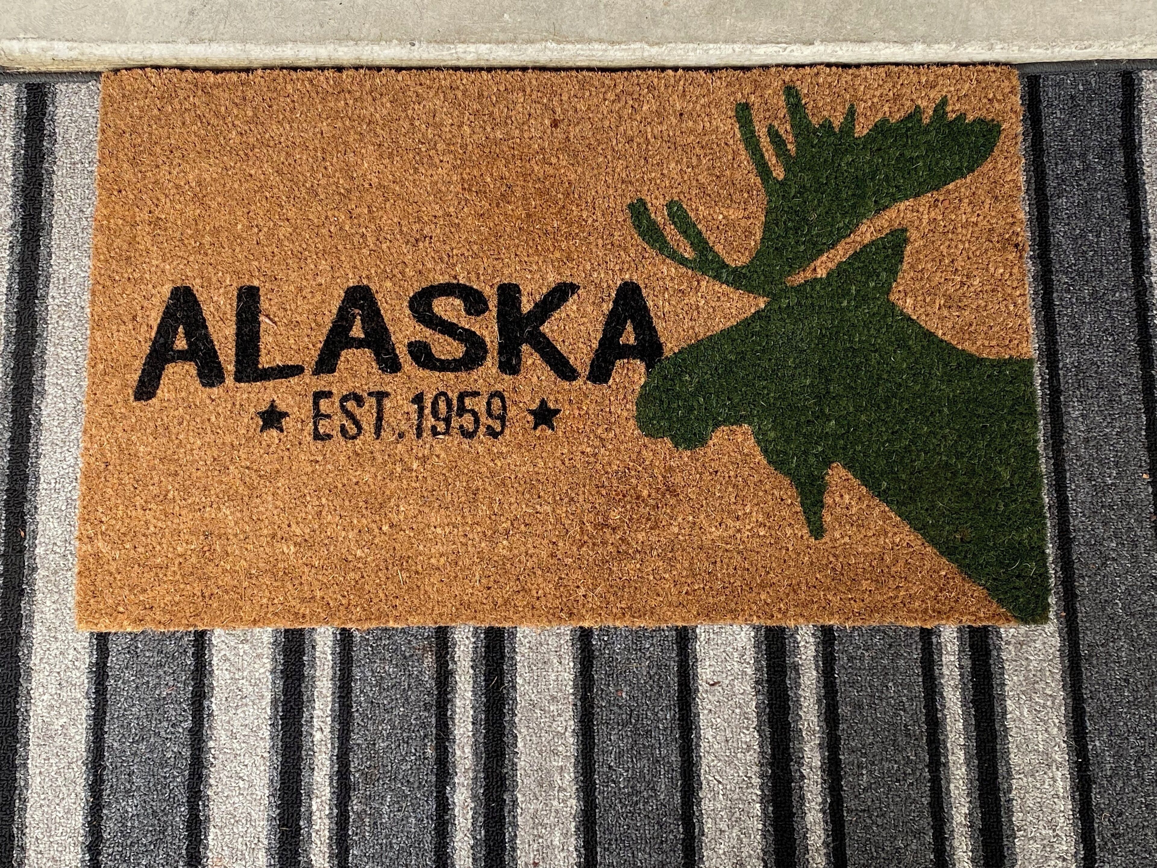 A doormat with "ALASKA" and a moose silhouette, and "EST. 1959" text.