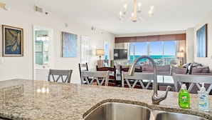 A modern kitchen with granite countertops, stainless steel sink, and a dining area with a view of the ocean.