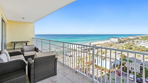A balcony with wicker furniture and a view of the beach and town.