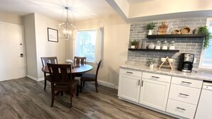 A modern kitchen with white cabinets, a brick backsplash, and a dining area with a wooden table and chairs. - Spacious & Cozy Unit in the Heart of Milwaukee (milwaukee)
