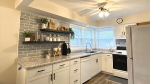 A modern kitchen with white cabinets, a granite countertop, a brick backsplash, and a ceiling fan. - Spacious & Cozy Unit in the Heart of Milwaukee (milwaukee)