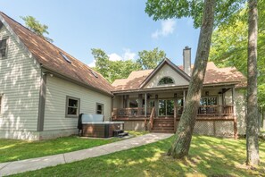 Una casa de dos pisos con un porche cubierto, un jacuzzi y una chimenea.