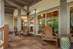 A wooden deck with Adirondack chairs, a wicker basket, and a green stool.