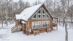 Una baita di legno con tetto spiovente, ampie finestre e un portico con ringhiera.