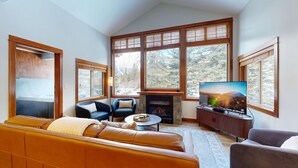 A modern living room with a fireplace, large windows, a sofa, and a television. - Stunning Ski In/Ski Out Getaway-Outstanding Views (Sun Peaks)