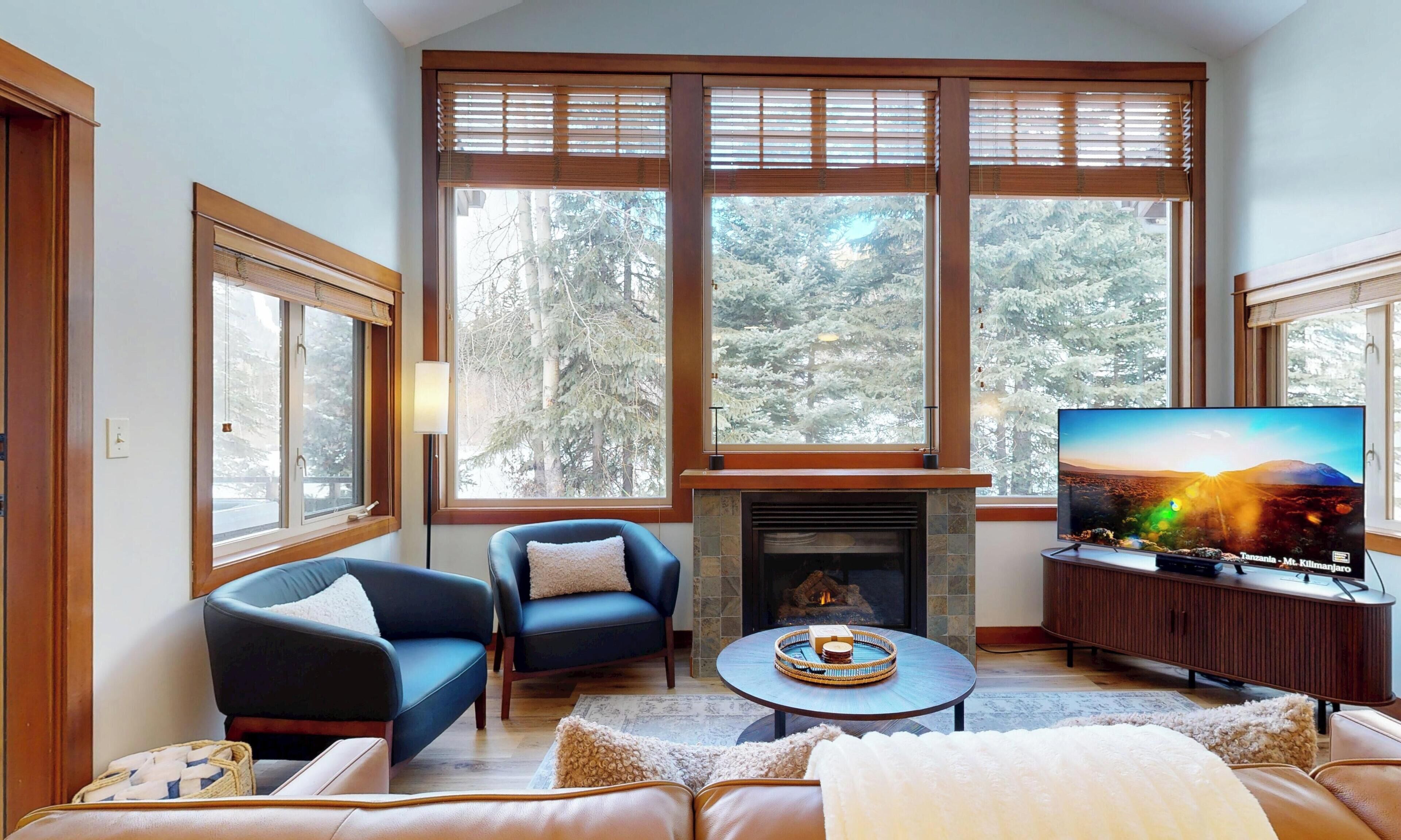 Una sala de estar con chimenea, ventanas amplias, un televisor y un rincón de descanso acogedor.