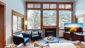 A living room with a fireplace, large windows, a television, and a cozy seating area. - Stunning Ski In/Ski Out Getaway-Outstanding Views (Sun Peaks)