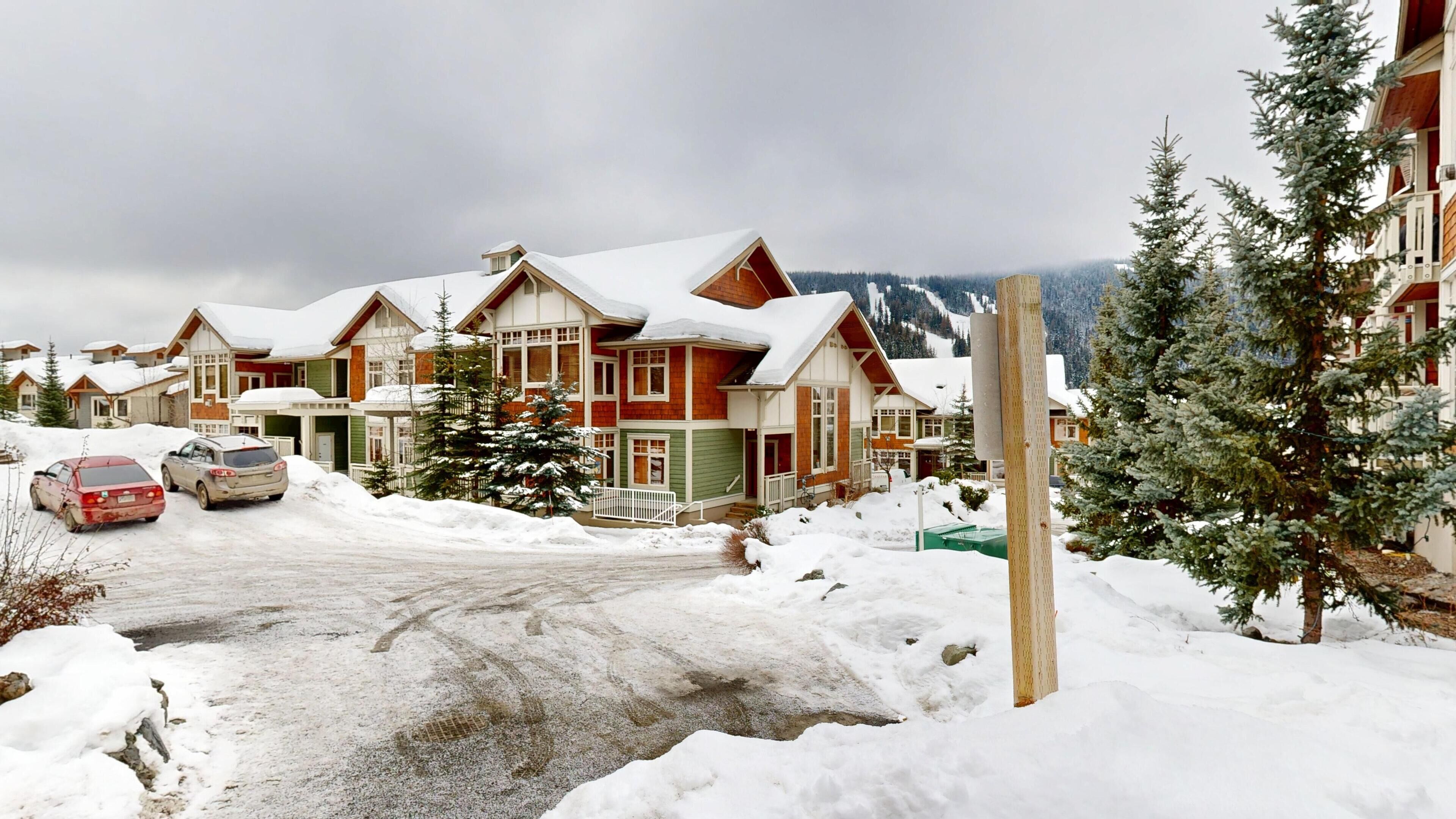 Un quartier résidentiel enneigé, avec des maisons, une route et une montagne en arrière-plan.