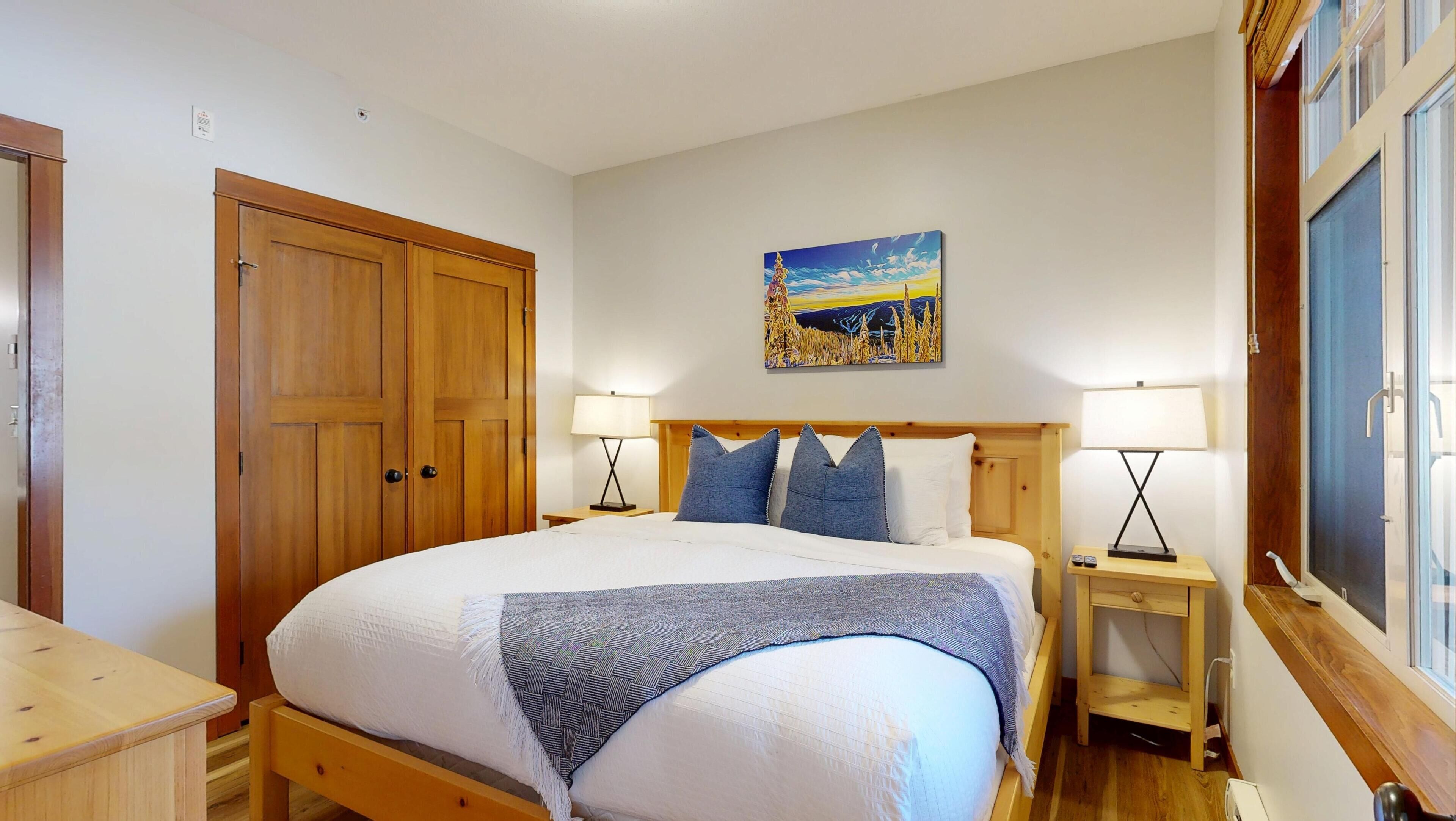 Une chambre à coucher avec un grand lit, une armoire en bois, deux tables de chevet avec des lampes et un tableau au mur.
