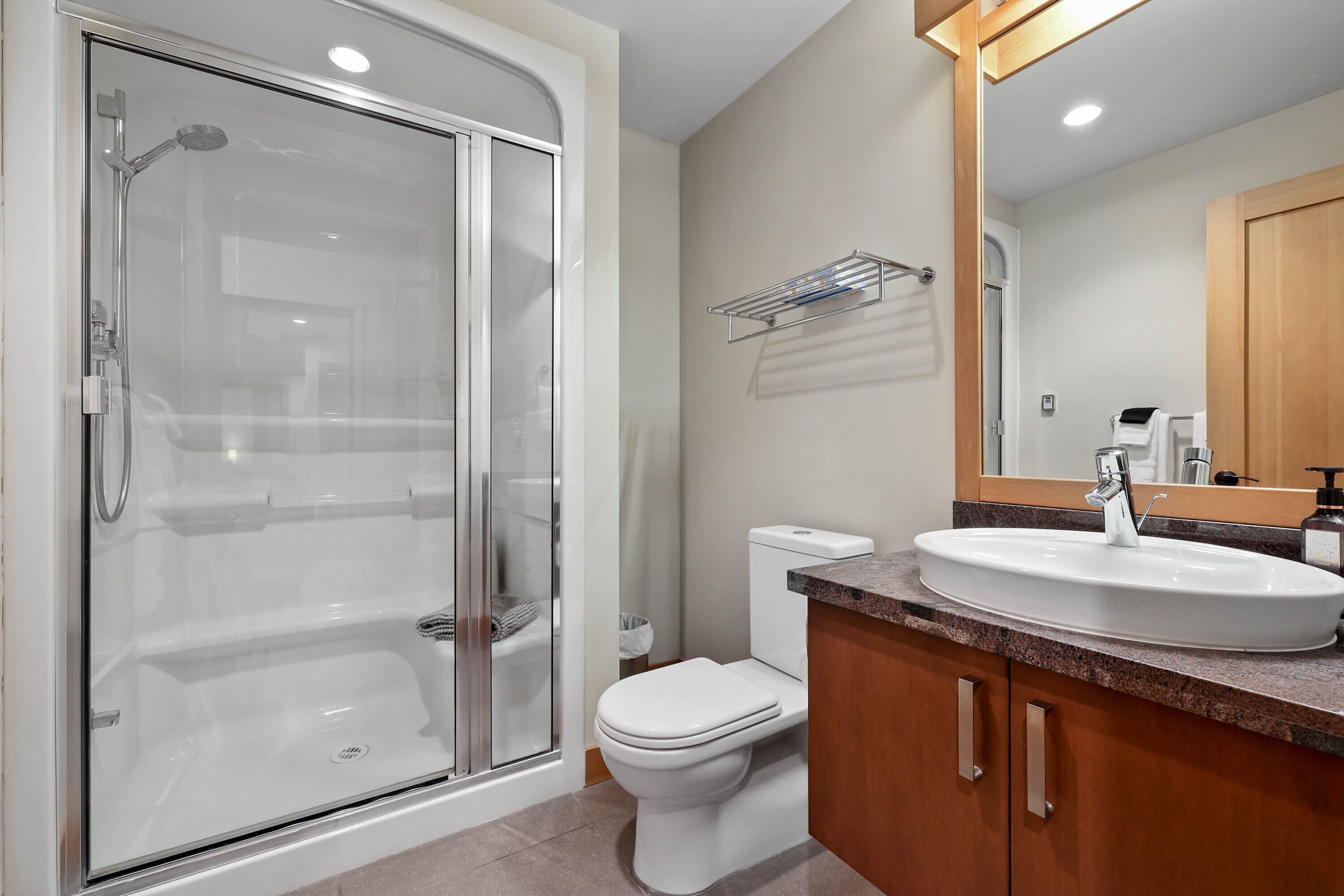 A modern bathroom with a glass-enclosed shower, a white toilet, and a sink with a wooden vanity.
