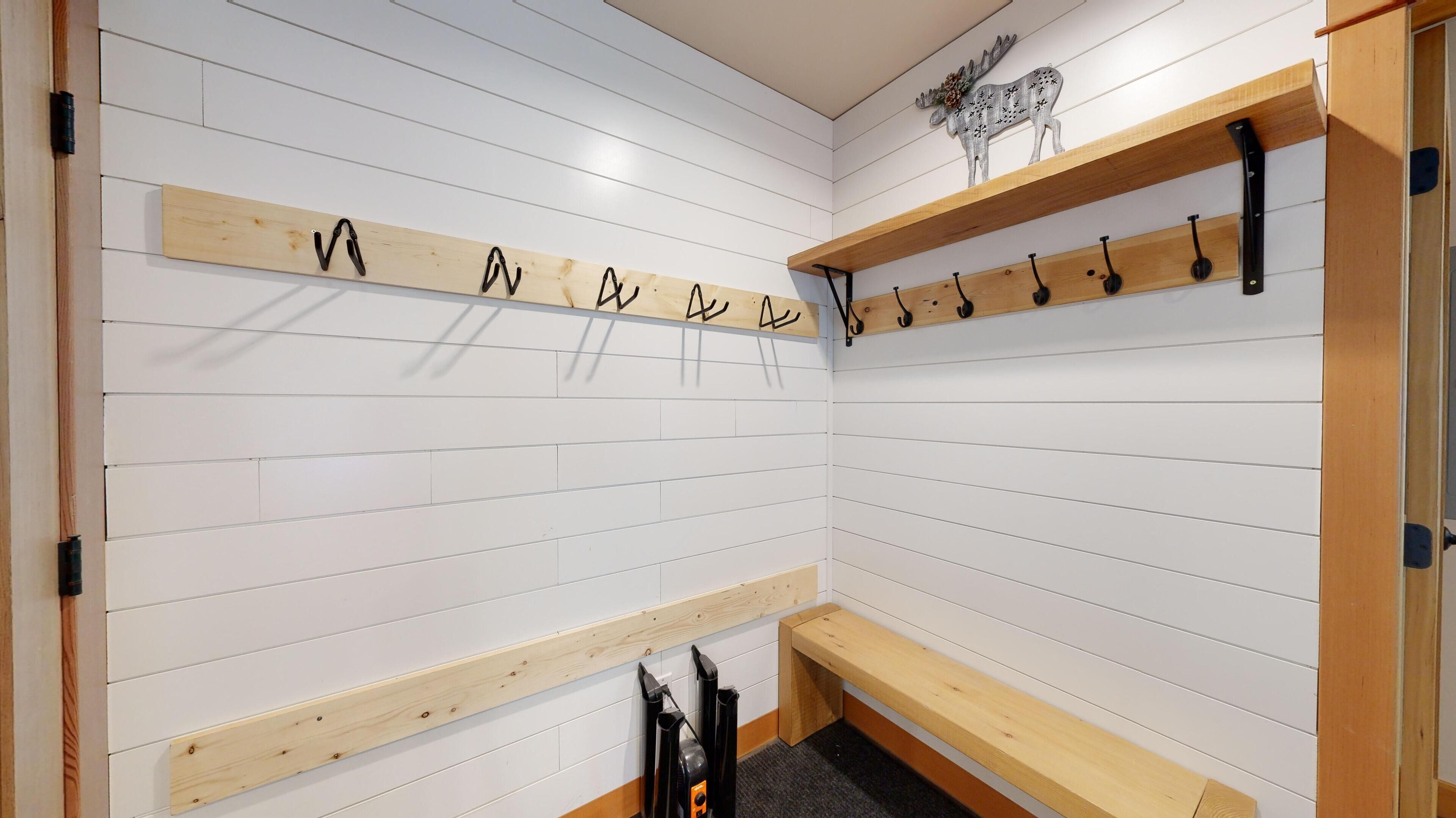 A room with white paneled walls, wooden shelves, and hooks for hanging items.