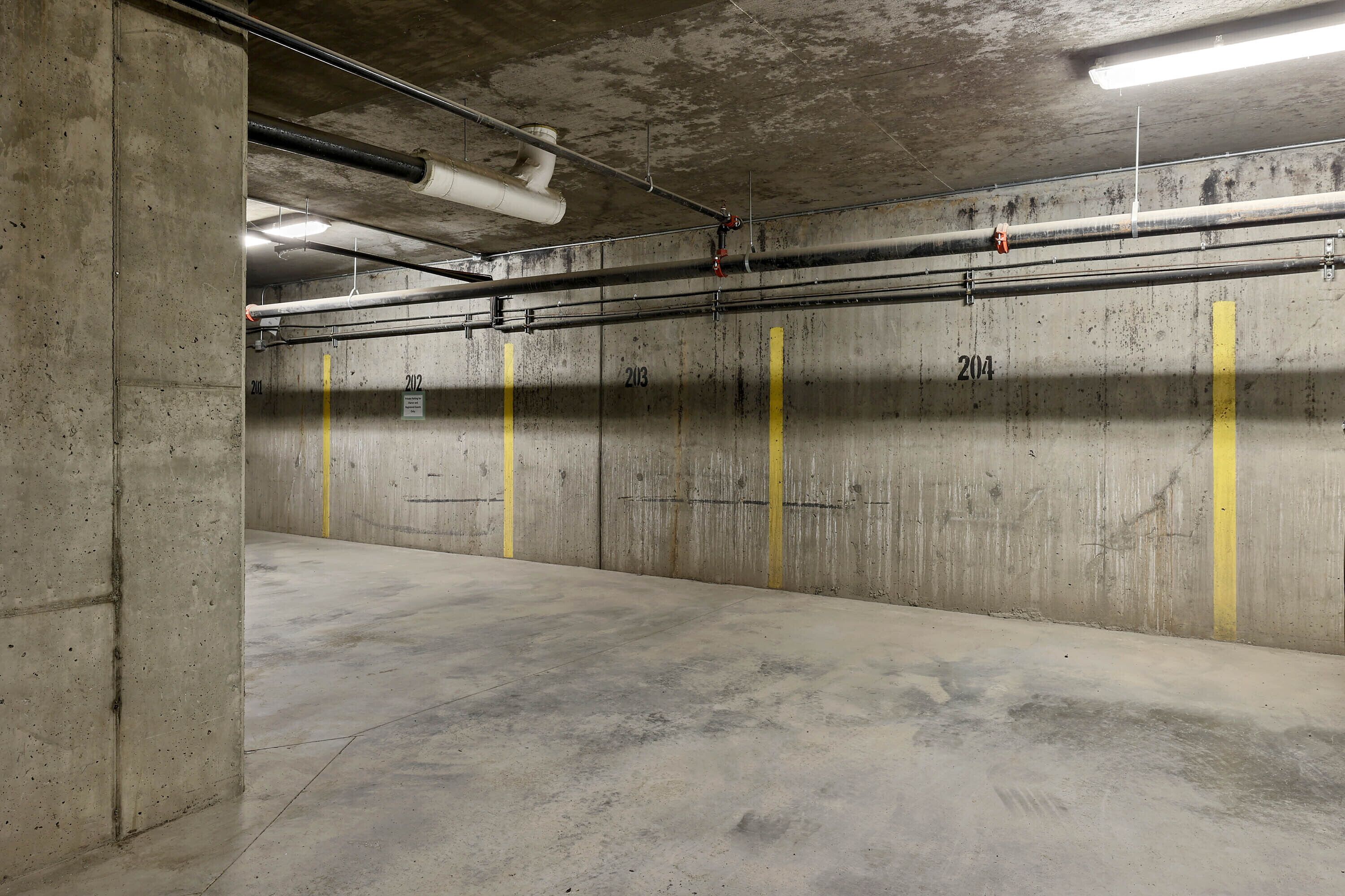 Un estacionamiento vacío con paredes de hormigón, espacios numerados y tuberías y conductos visibles.