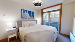 A hotel room with a bed, a nightstand, a lamp, a wall-mounted artwork, and a sliding glass door leading to an outdoor area. - Spacious Ski in/out Condo in Sun Peaks Village (Sun Peaks)