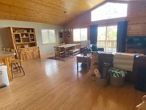 Uma sala de estar espaçosa, com piso de madeira, uma mesa de jantar com cadeiras, um sofá e uma televisão.
