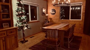 A cozy dining area with a wooden table and chairs, a Christmas tree, and a chandelier.