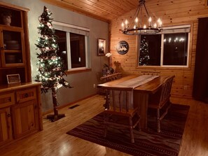 A cozy dining area with a wooden table and chairs, a Christmas tree, and a chandelier. - Book Your Big Bear Ski Vacation at Serenity Peak, Upper Moonridges' Finest (Big Bear City)