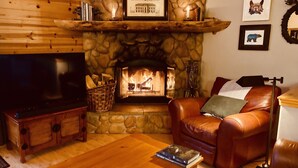 A cozy living room with a stone fireplace, leather sofa, wooden coffee table, and a flat-screen TV.