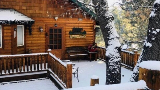 A wooden cabin with a porch, a bench, and a signboard.
