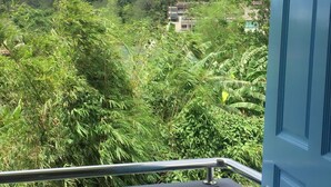 A balcony with a view of a lush green hillside and a building in the distance. - Fahsai Hotel Aonang (Krabi)