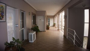 Un pasillo con puertas numeradas 203 y 202, plantas en macetas y suelo de baldosas.