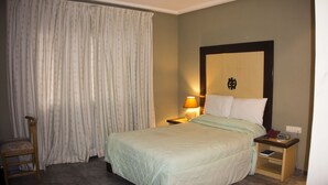 Una habitación de hotel con cama, mesita de noche, silla y cortina.
