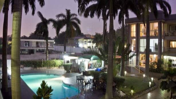 Un resort con piscina, palmeras y un edificio bien iluminado de varios pisos.