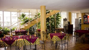 Un restaurante con varias mesas y sillas, una escalera y amplias ventanas.