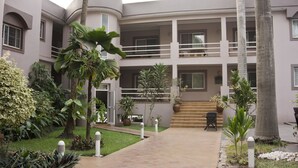 Un hotel de varios pisos con un patio central, que cuenta con una escalera, palmeras y diversas plantas en macetas.