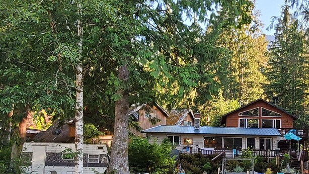 Une cabane dotée d’une terrasse et d’un espace extérieur aménagé, le tout entouré d’arbres.