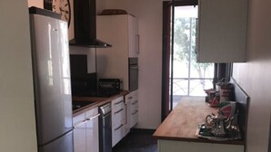 A compact kitchen with white cabinets, a stainless steel refrigerator, a built-in oven, and a coffee maker on the counter.