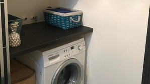 A compact laundry area with a washing machine, a blue basket on a shelf, and a small wooden cabinet.