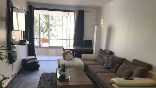 A living room with a sofa, a coffee table, and a TV. There is a window with curtains, a plant, and a chair.