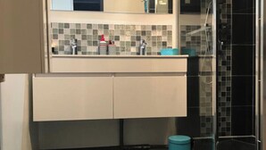 A bathroom with a tiled backsplash, a mirror, a sink, and a shower area.