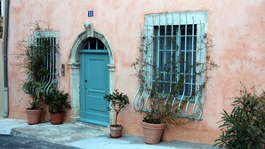 Un bâtiment avec une porte bleue et deux fenêtres grillagées. Des plantes en pot sont placées devant la porte et les fenêtres.