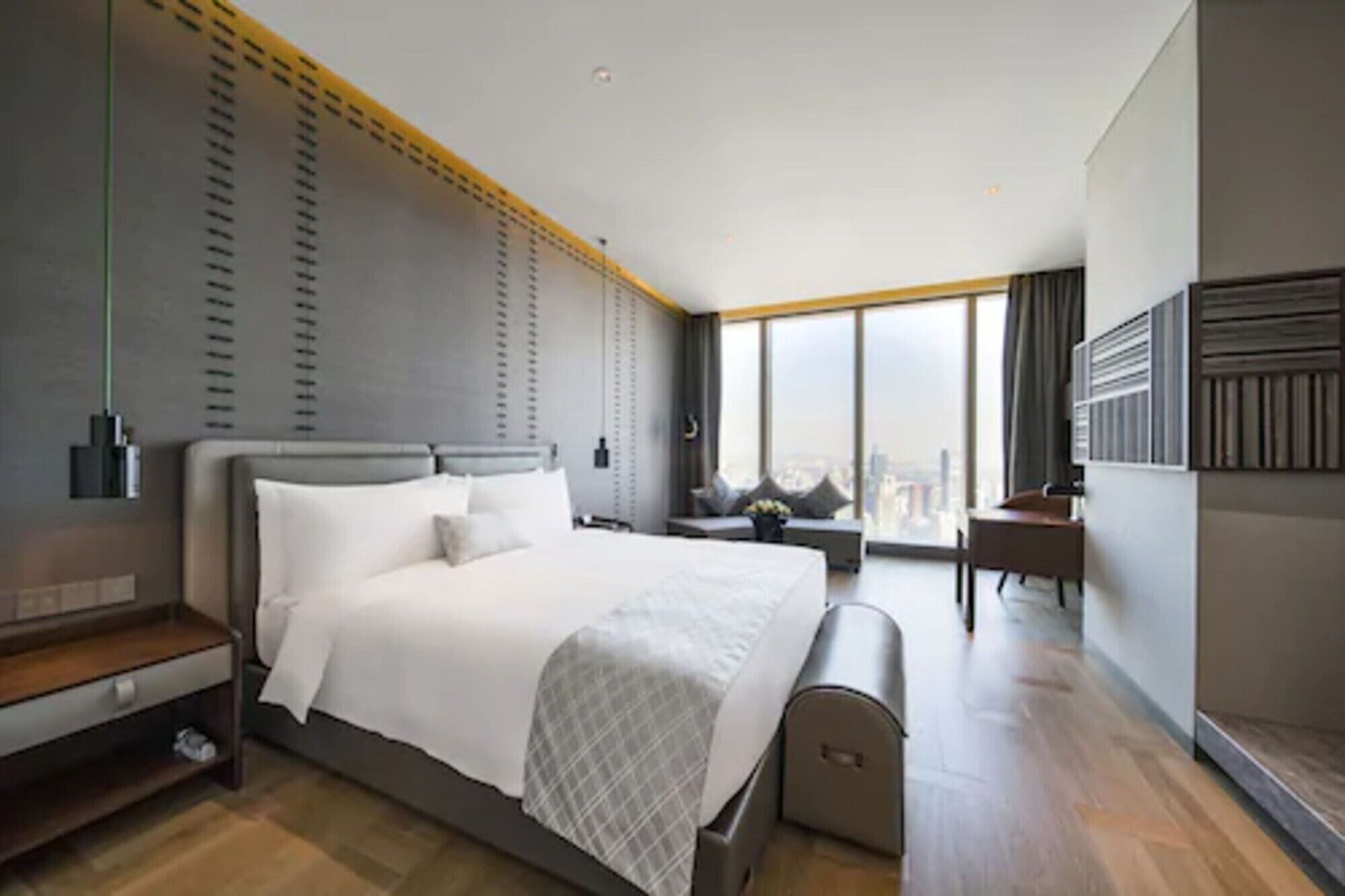 A modern hotel room with a large bed, a desk, and a view of the city.