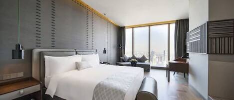 A modern hotel room with a large bed, a desk, and a view of the city.