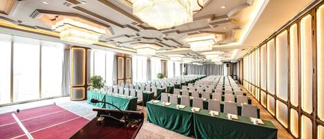 Une salle de conférence avec des rangées de tables, un grand lustre et de grandes fenêtres.