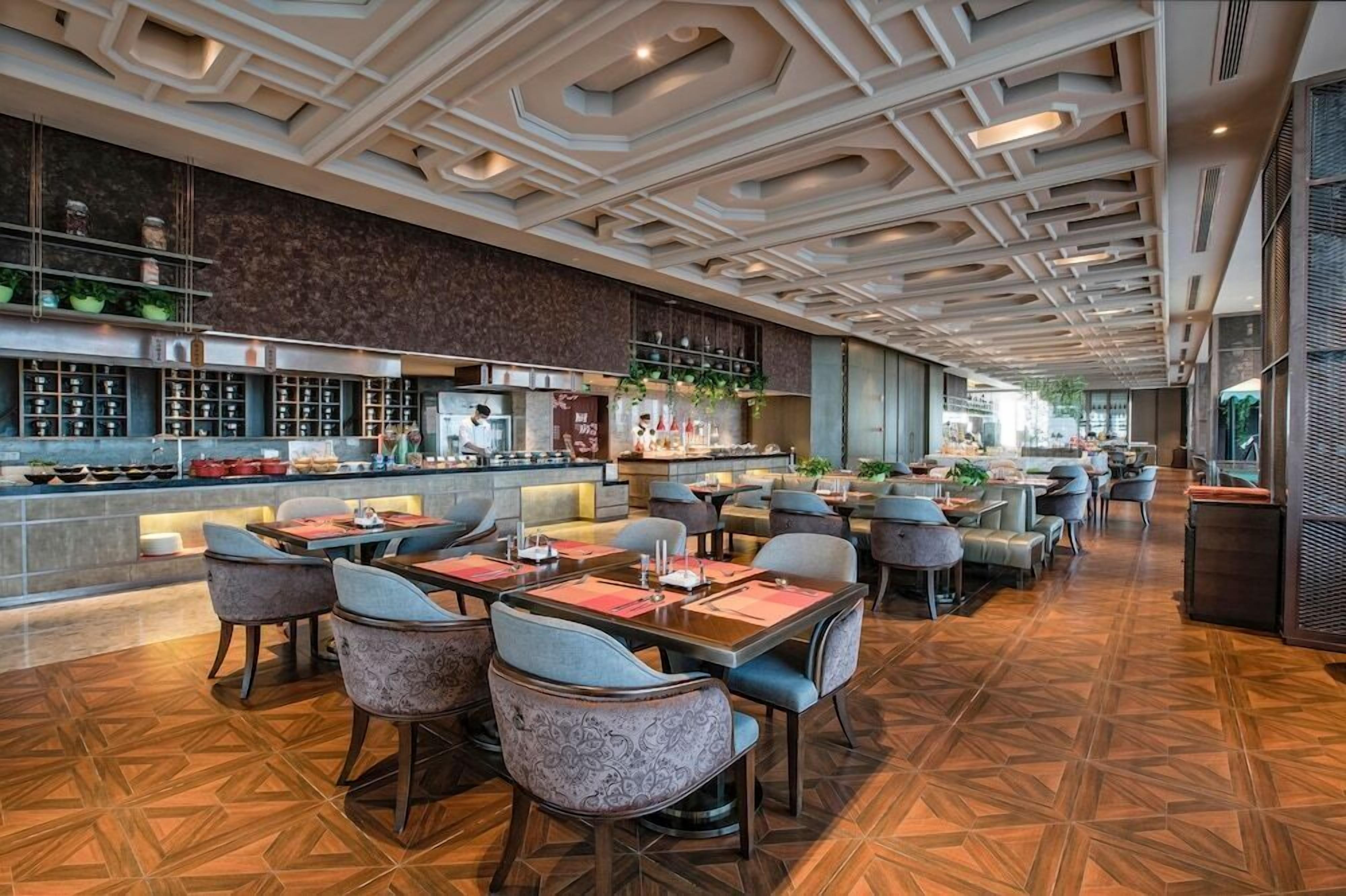 A modern restaurant with a geometric ceiling design, a bar area, and a variety of seating options including tables and chairs.