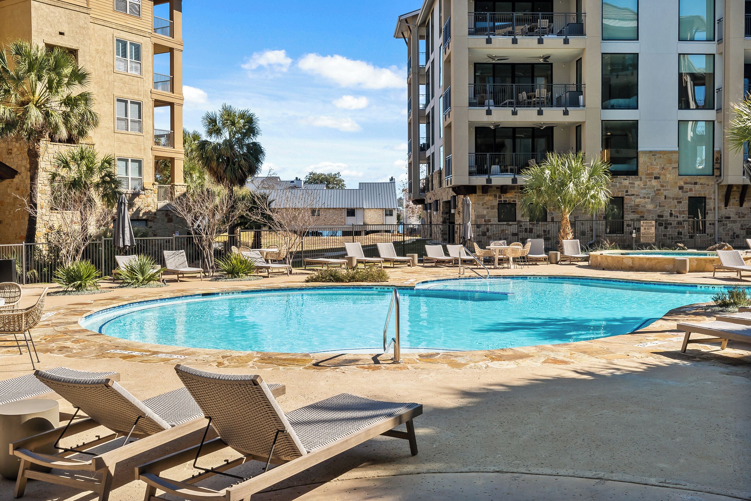 Une piscine avec des chaises longues, des palmiers et un immeuble à plusieurs étages doté de balcons.