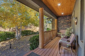 Una terraza de madera con un muro de piedra, una silla de mimbre y una pequeña mesa.